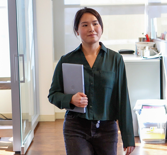 aleana walkin through the office, holding a laptop