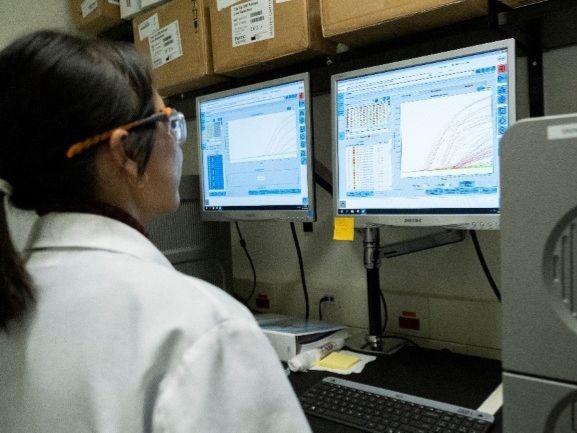 A technician wearing a lab coat and safety glasses confirms parameters on a screen