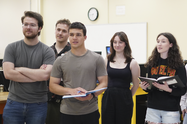 group of students standing with books open watching a presentation