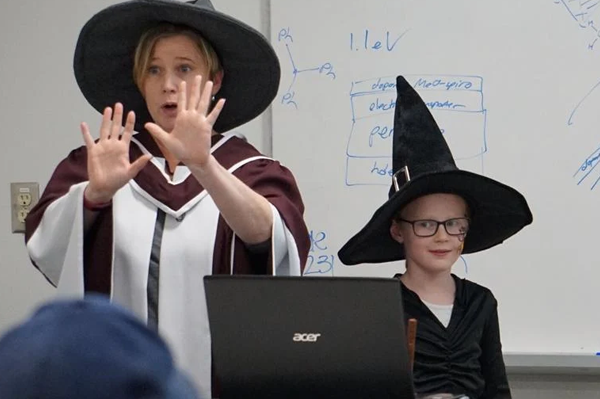 a woman and a girl dressed up as witches, in a classroom