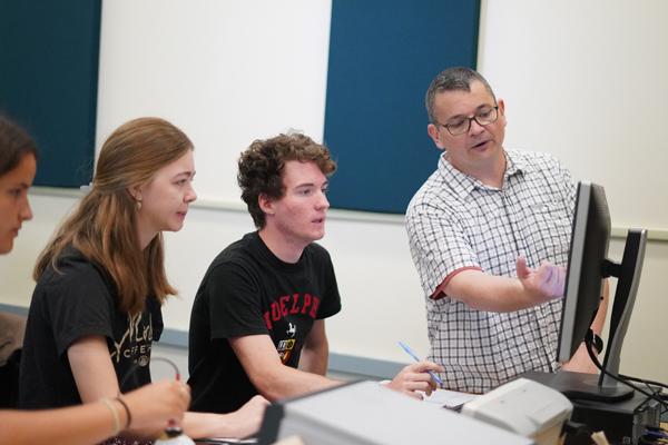 Instructor pointing out information on computer screen to a group of 3 students