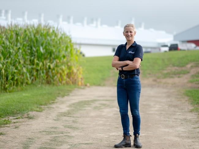 Dr. O'Sullivan stands outside in a golf shirt, jeans and boots, in front of the Ontario Swine Research Centre