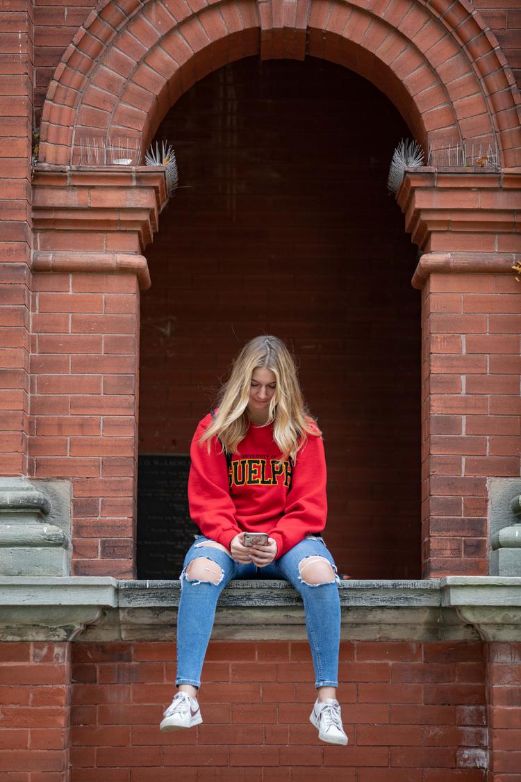 Person in a Guelph sweater sitting looking at her phone.
