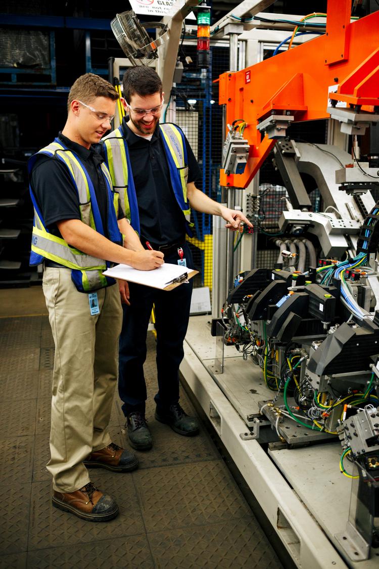 two people in yellow vests examining engine in factory