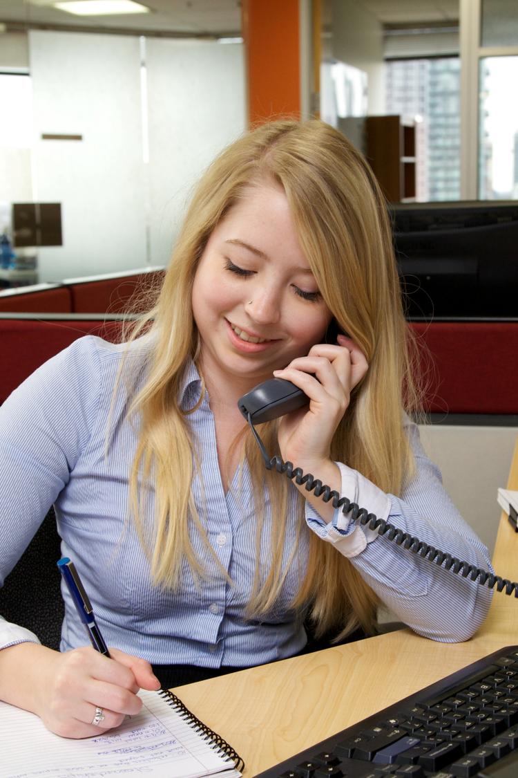 person writing on notepad while on the phone in an office