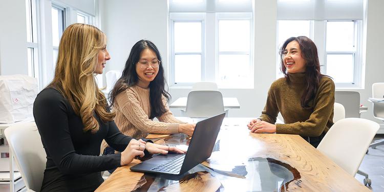 Group of 3 female students working a laptop in an office meeting room.