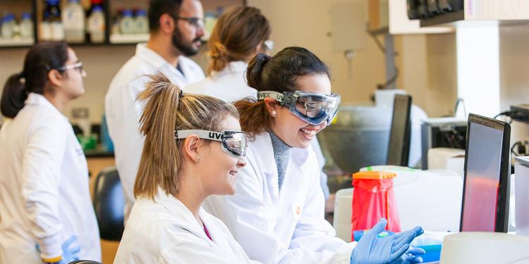 Students in lab coats and goggles working in a lab.