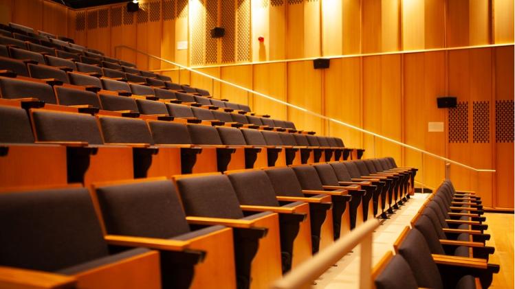 Image of arts research centre auditorium with rowed seating, wood paneled walls and warm lighting
