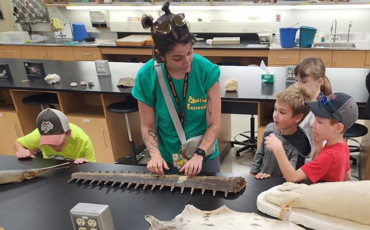 A volunteer and 4 children at a Creative Encounters aquatic lab looking at a bone in awe.