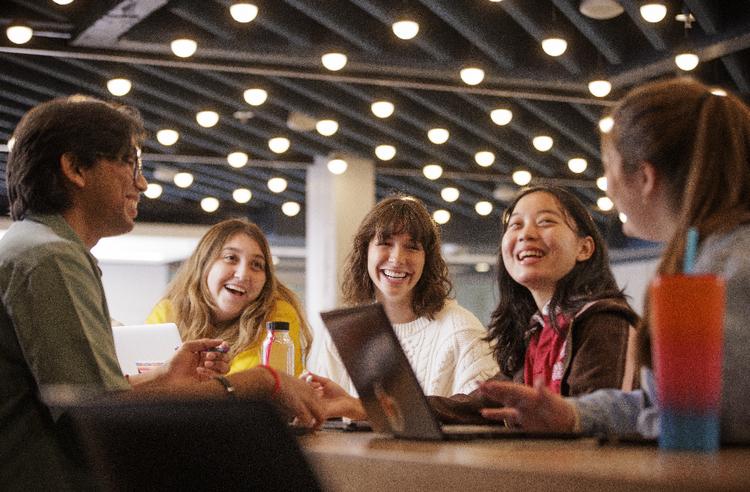 A group of students gathered around a table, laughing during conversation.