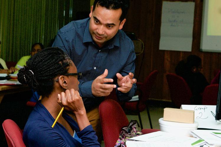 Professor leans down to speak with student working at a table