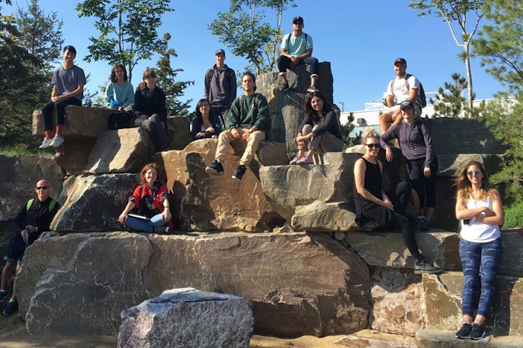 12 students pose outside on large rocks.