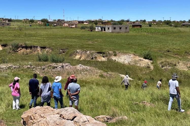 Group of people look out onto a grassy and rocky South African landscape 