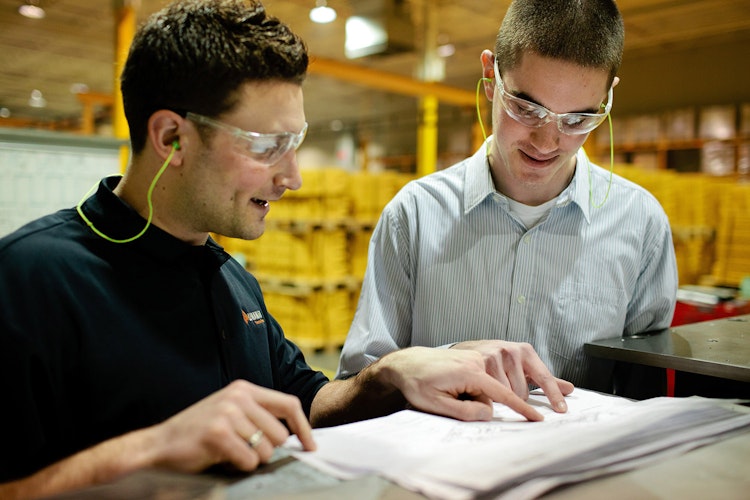 Employer and student in safety glasses discuss notes