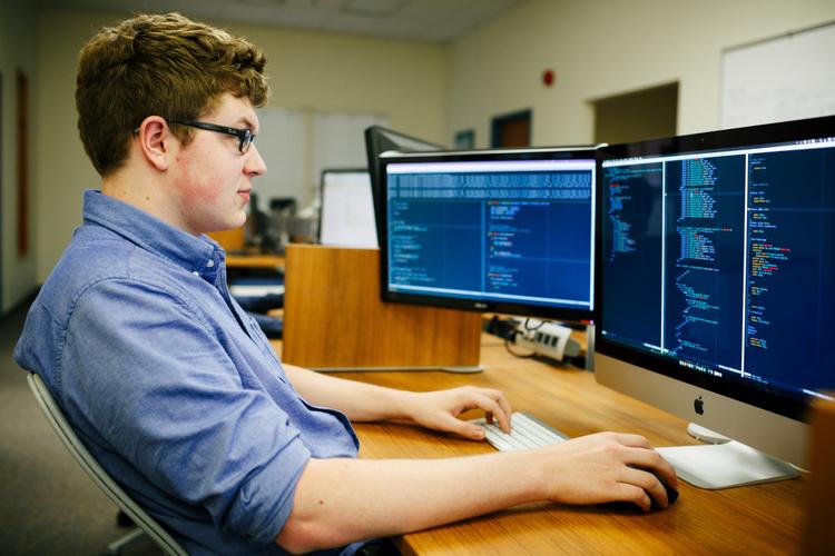 Person looks at two computer screens, with code on them.