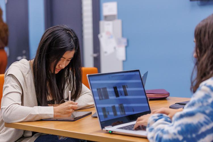 Two students in Reynolds building doing coursework on their laptop and tablet.