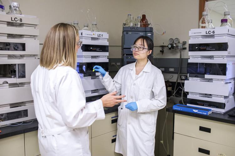 Two scientists in lab coats engaged in a conversation, sharing insights in a professional laboratory setting.