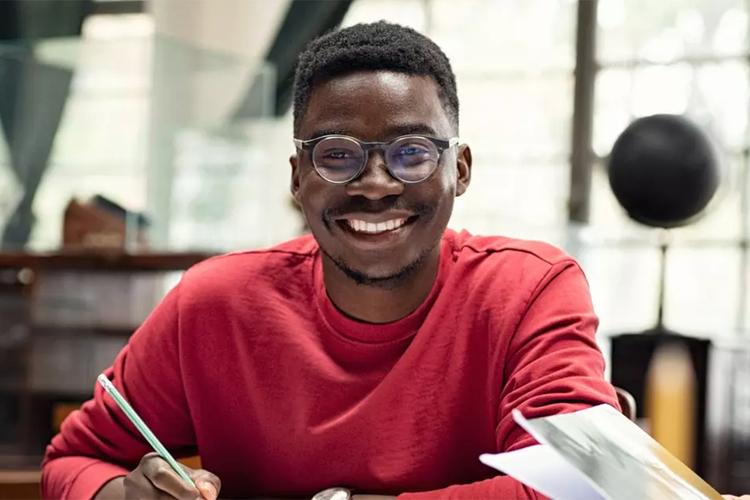 U of G student sitting at a desk with pencil in hand smiling at the camera