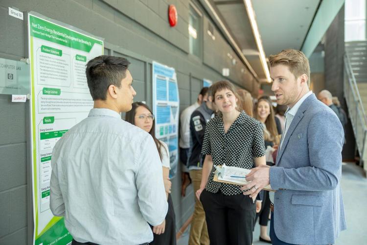 a judge speaking to a presenting group of students in front of their project poster