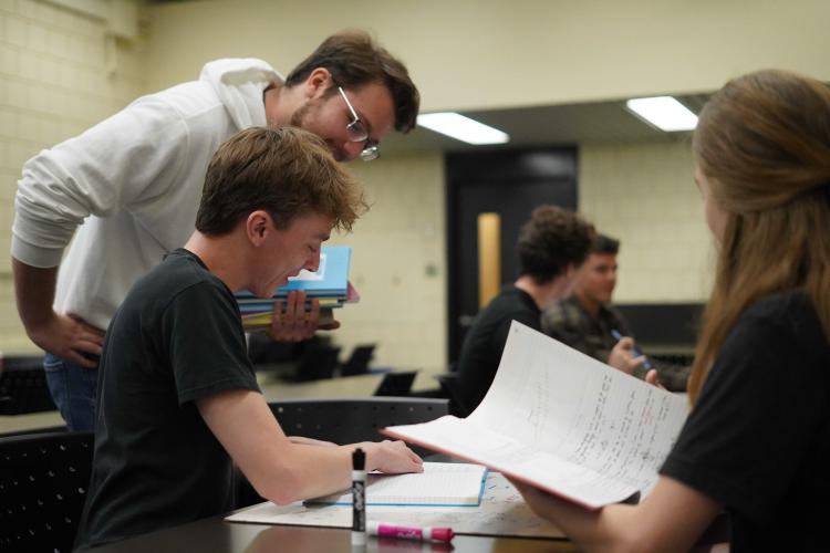 A professor is looking over a students shoulder offering guidance.