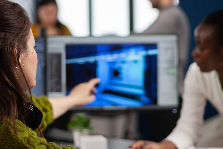Individual pointing at a computer screen while speaking to a colleague.