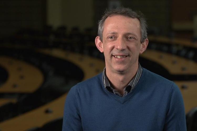 Bédécarrats, wearing a collared shirt and sweater, sits smiling for an interview