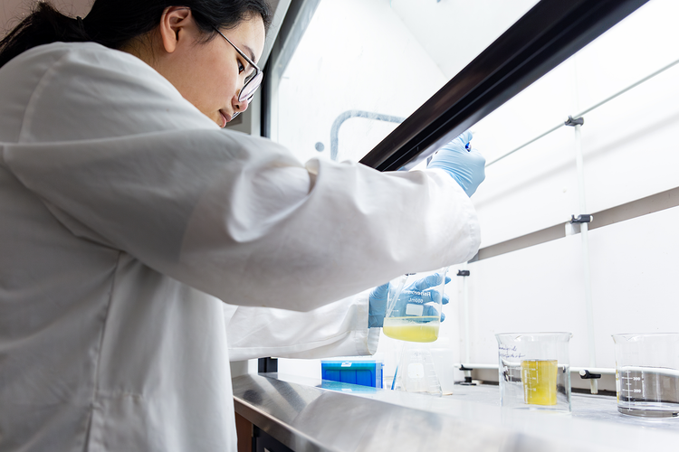 student in a lab working with a solution in a beaker