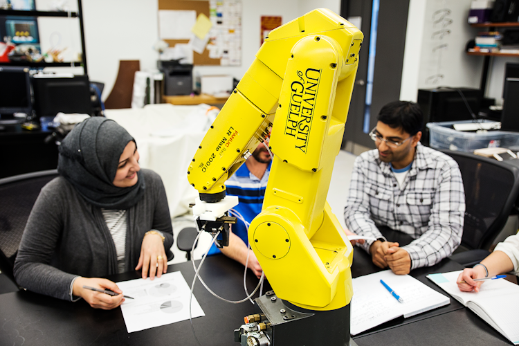 a group of grad students gathering around a robotic arm