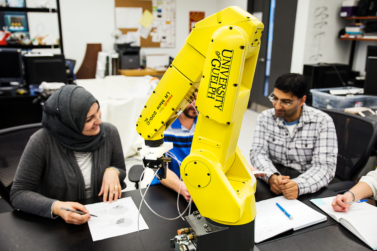 a group of grad students gathering around a robotic arm