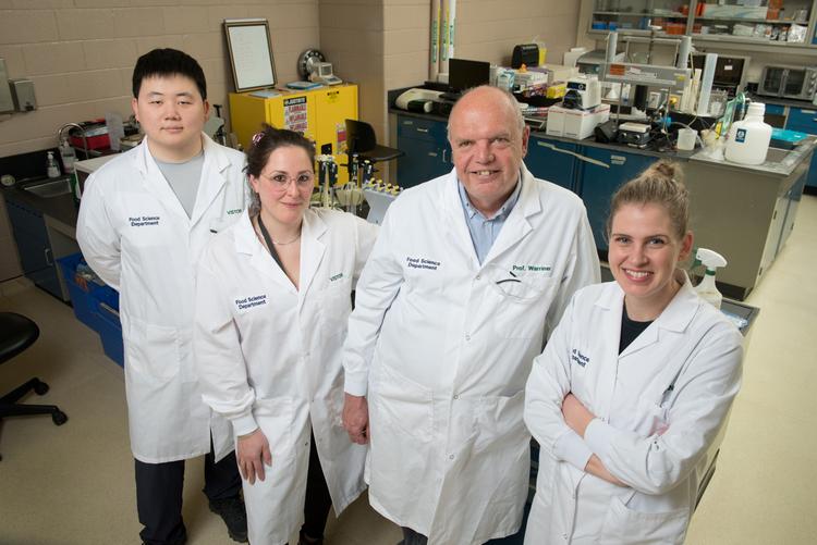 Warriner, two students and the lab manager wear lab coats and smile in their food science laboratory