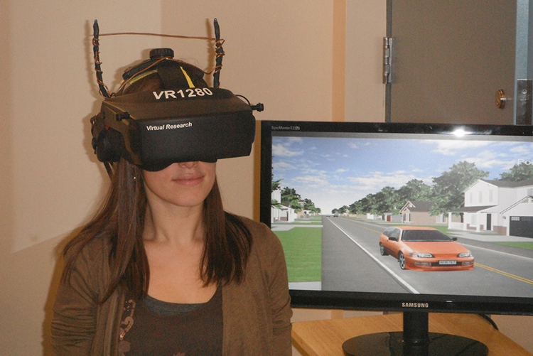 Woman wearing Virtual Reality headset with monitor in background displaying traffic view