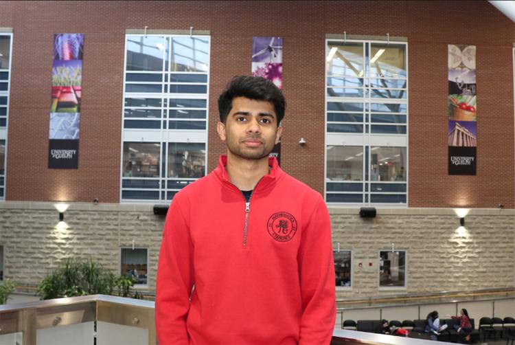 Vinay Joshy wears a University of Guelph sweater and stands in the Summerlee Science Complex