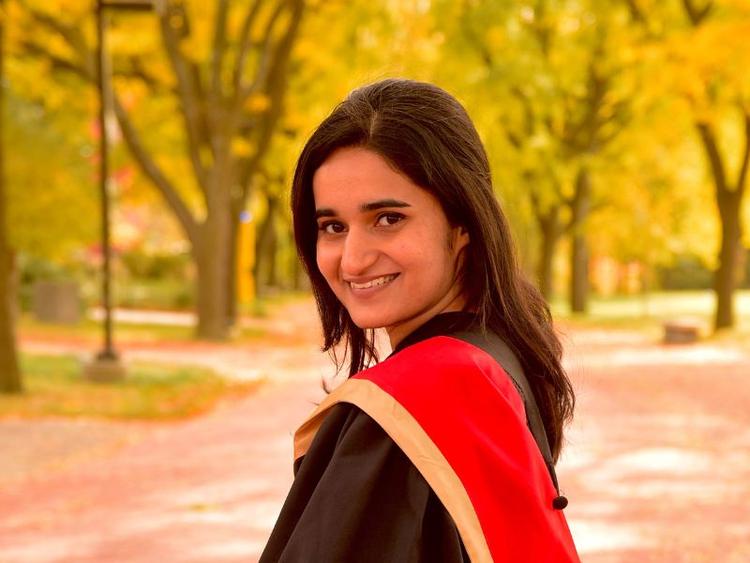 Microbiology Grad Parneet Kaur posing outside in her grad gown.
