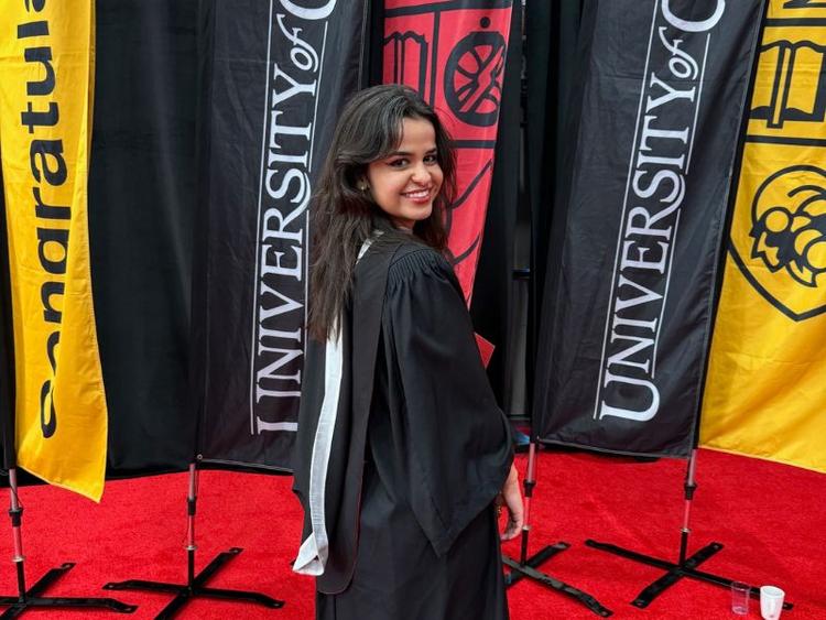 U of G Grad Julia Moraes wearing a grad godwn and posing in front of U of G banners at her graduation.