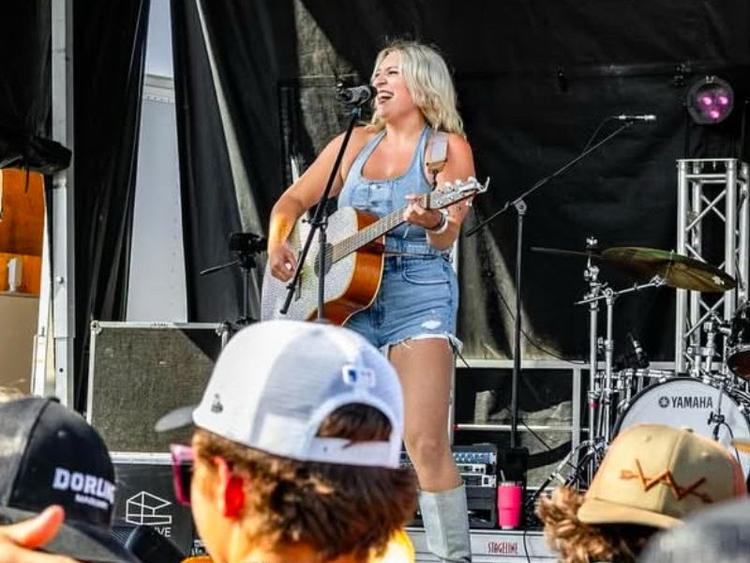 Paige Rutledge playing a guitar while performing at a live music venue.