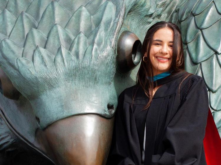Guelph Grad Lauren Yee posing in her grad gown by the Gryphon statue.