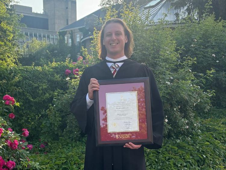 Image of U of Guelph Philosophy Grad Michael Lanc posing with his degree.