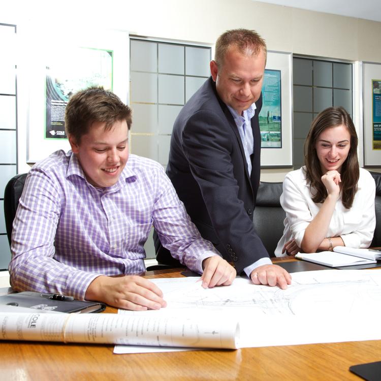 2 co-op students sit at a table, while employer points out something on a document.