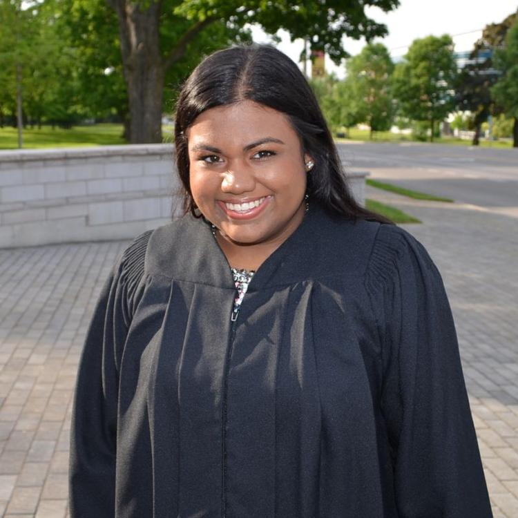 Dr. Naythrah Thevathasan in her grad gown in front of the University of Guelph.