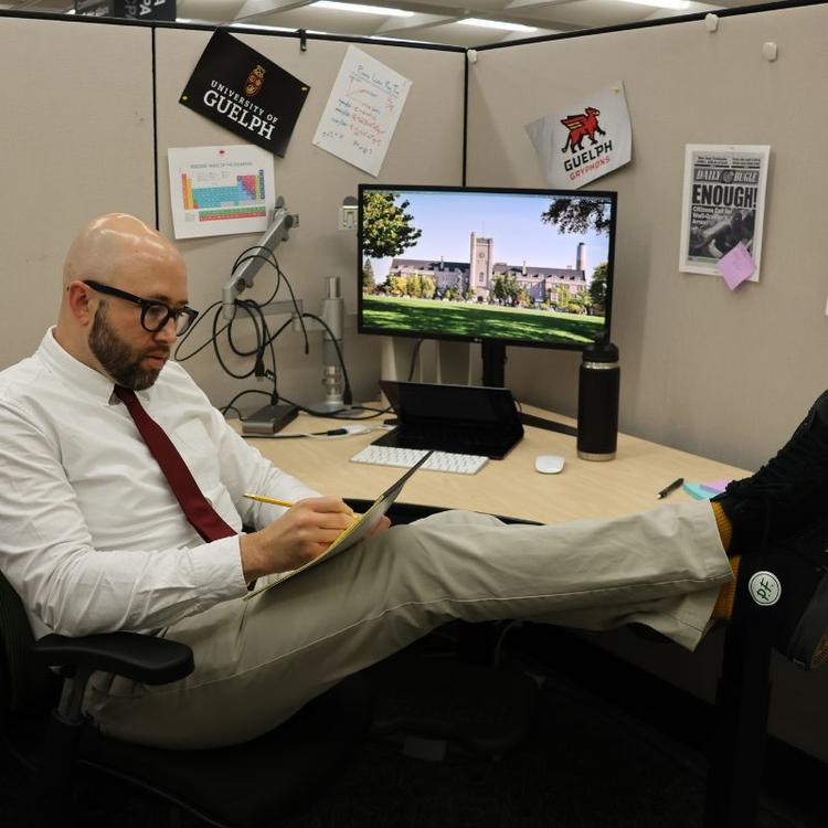 GradCast host sitting at his desk while writing on a pad of paper.