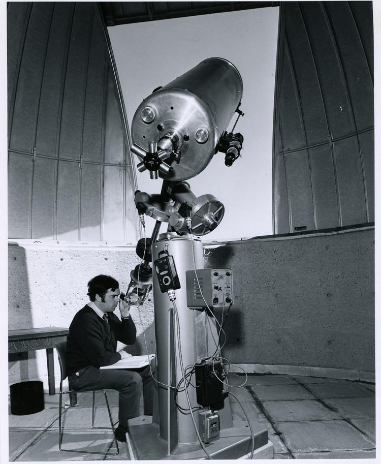 black and white, man seated at a large telescope with the observatory dome open
