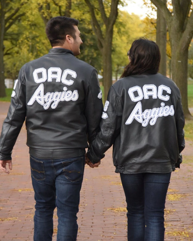 A back shot of two people holding hands wearing their OAC Aggies jackets.