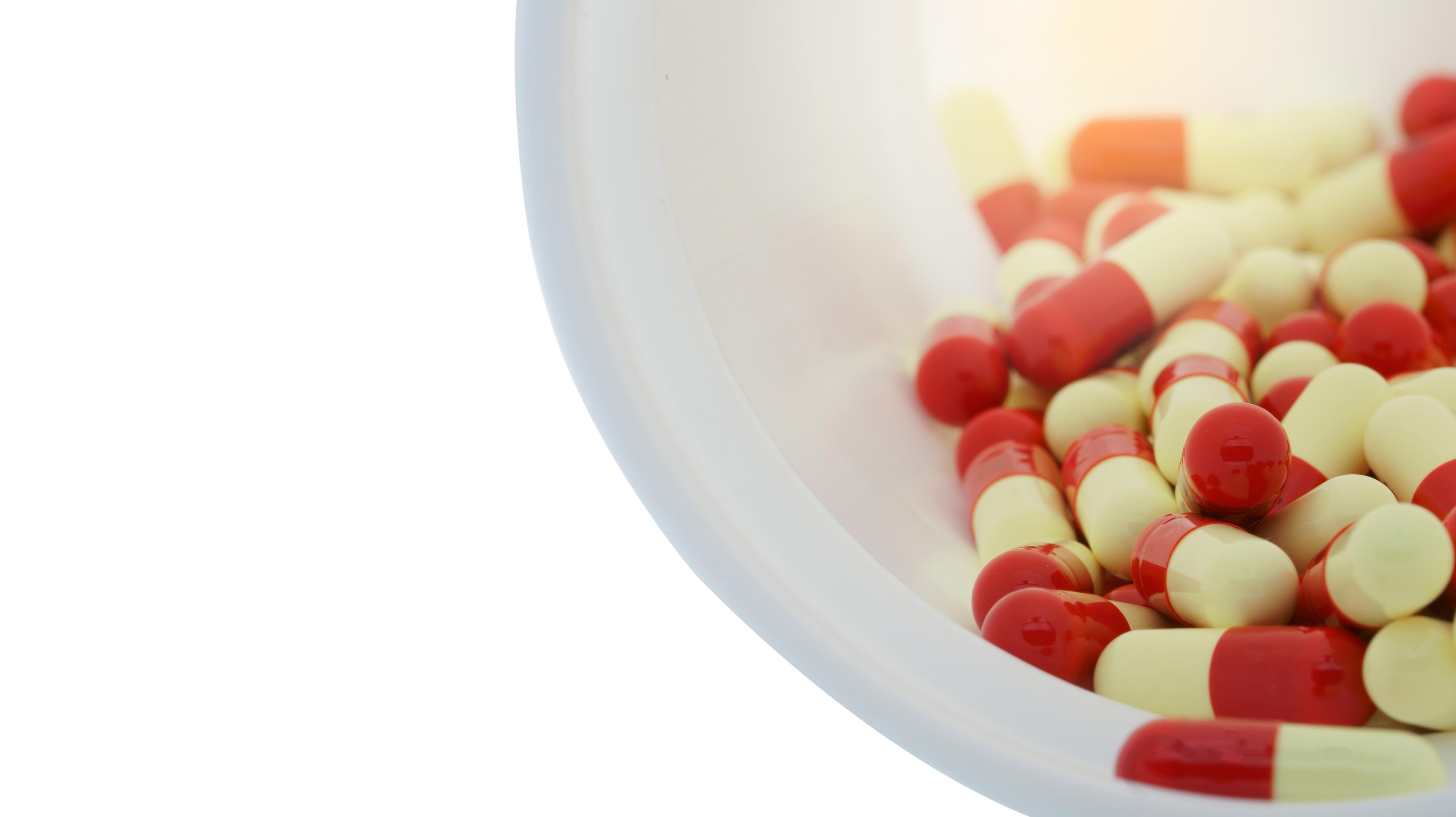 Red and white pill capsules spill out of a white bottle.