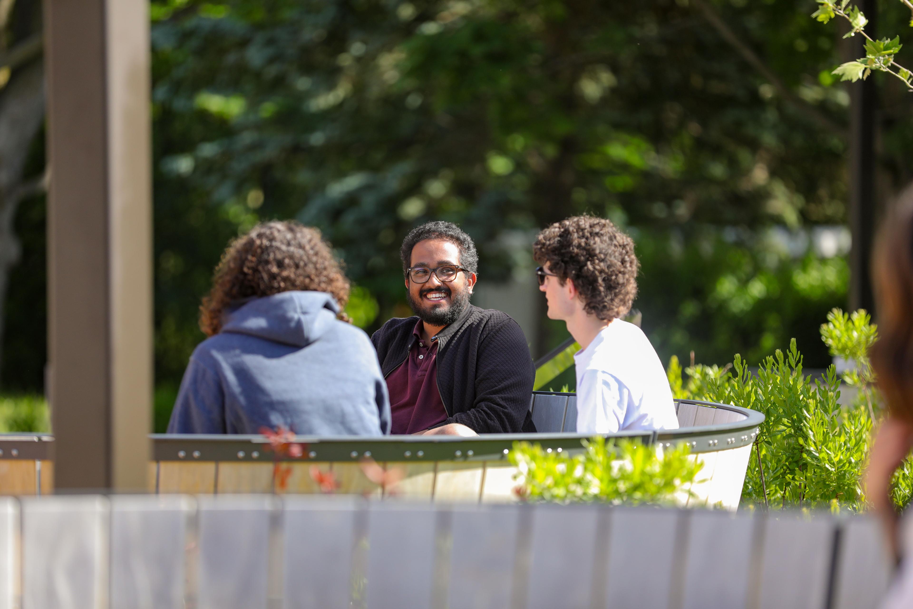 Three business students sitting in Lang Plaza on a bench.
