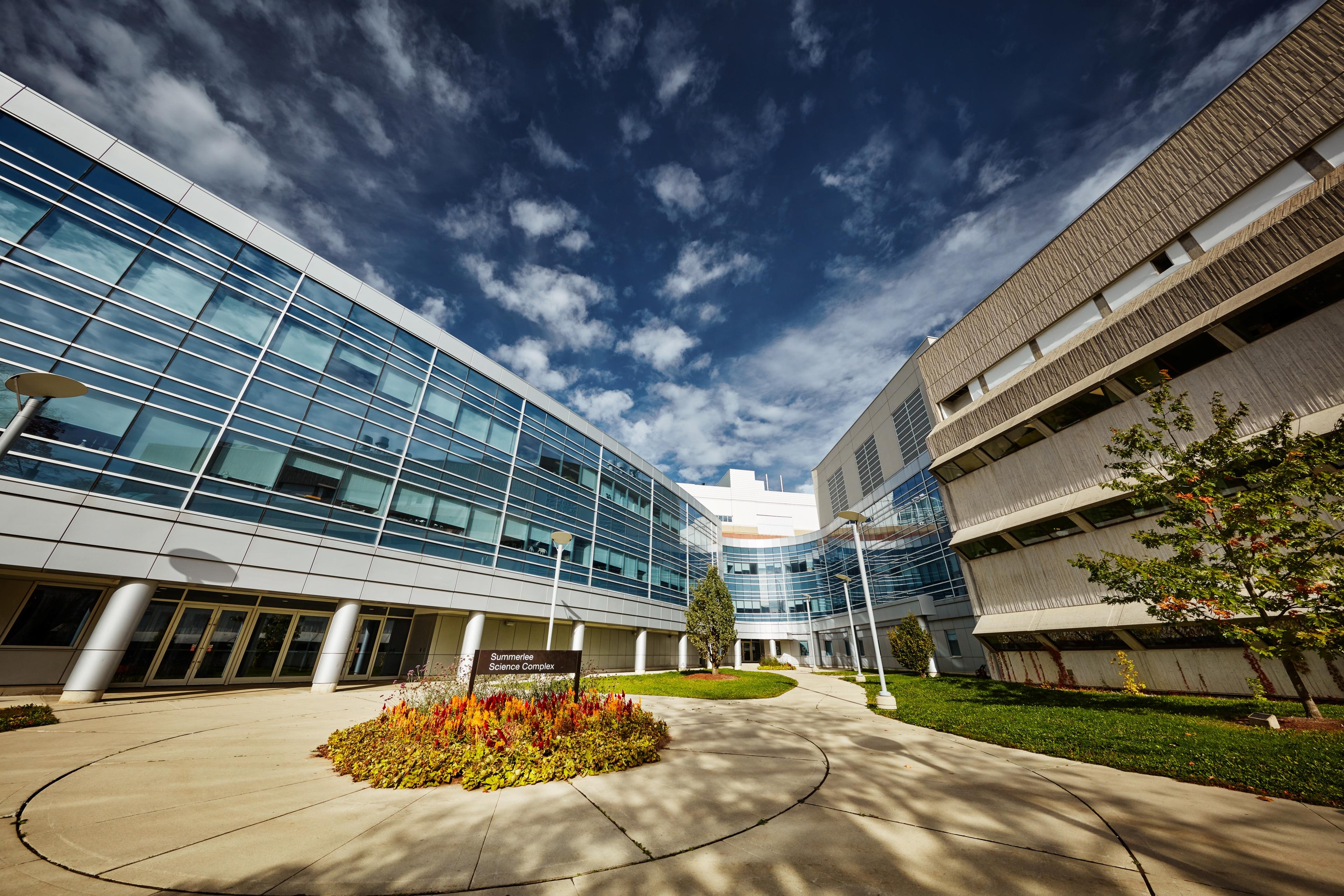 Outside shot of U of G campus. Summerlee Science Complex is on the left - glass windows blue colour. MacNaughten is on the right, grey concrete.