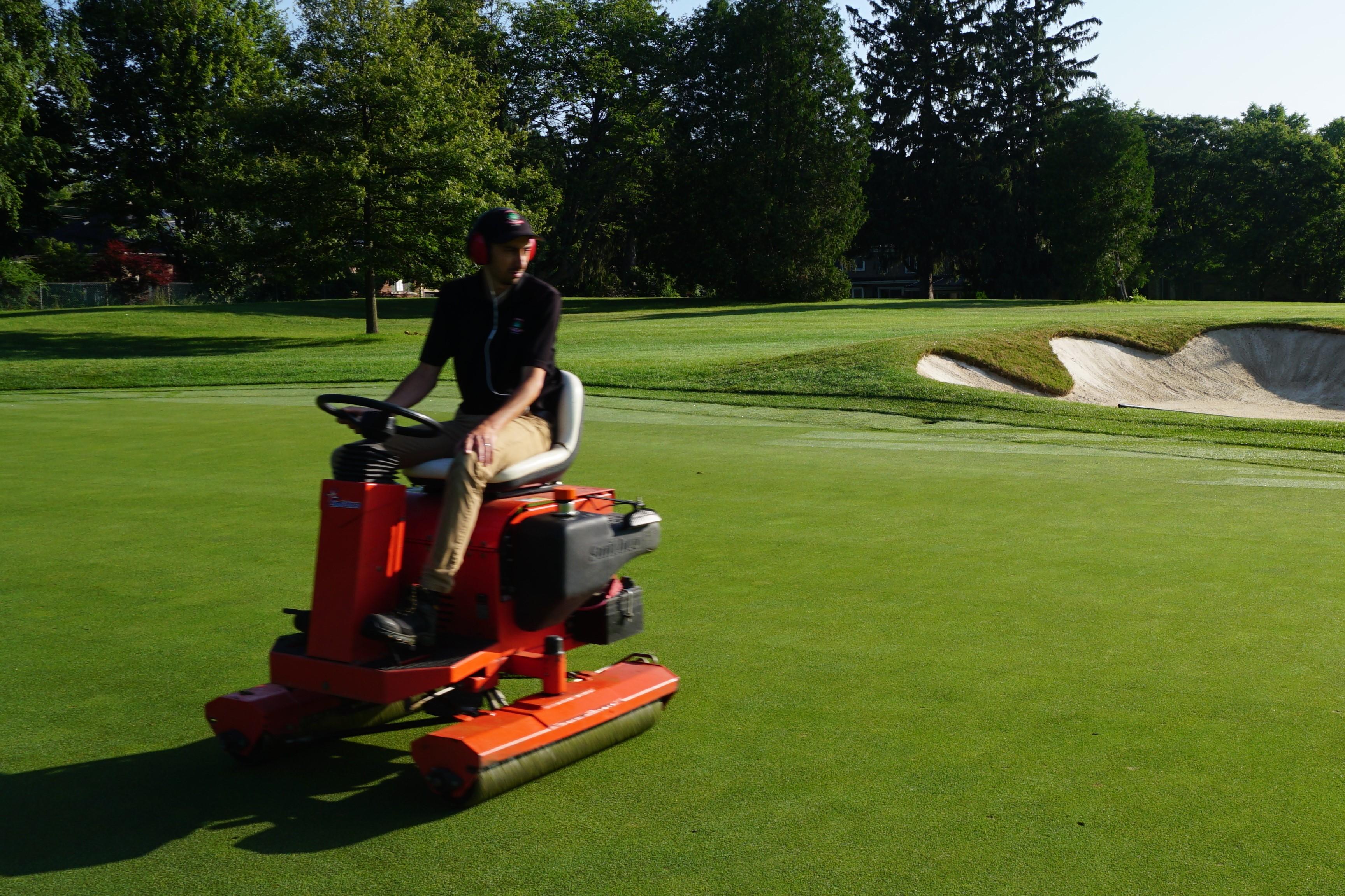 person driving greens roller on turfgrass