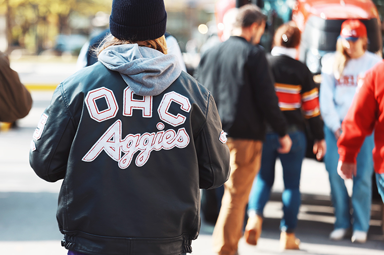 a student wearing a leather jacket outside with other students in the background