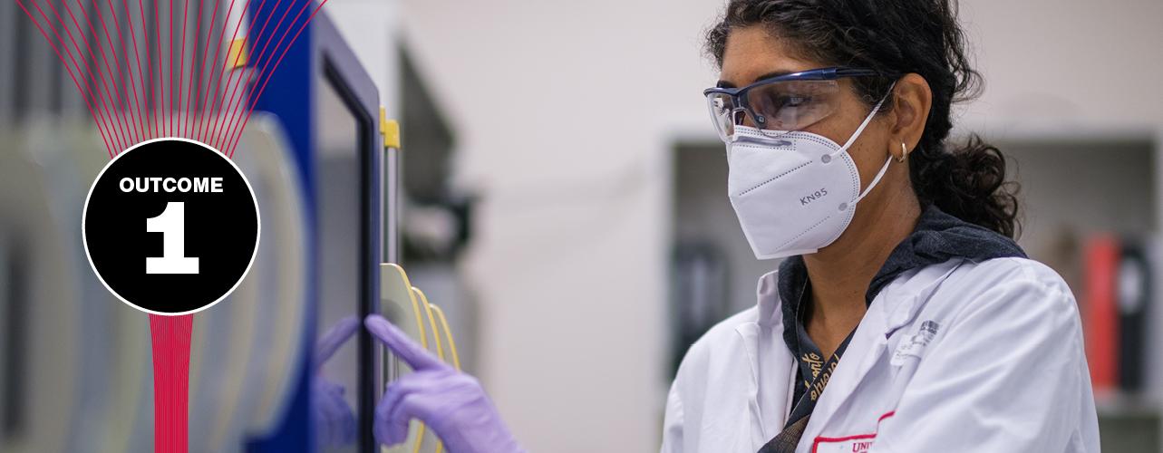 A laboratory technician in a lab coat, face mask and eye protection