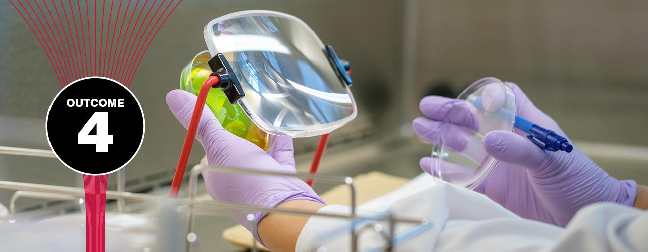 Close-up of a lab technician’s nitrile-gloved hands holding a petri dish behind a rectangular mounted magnifying glass
