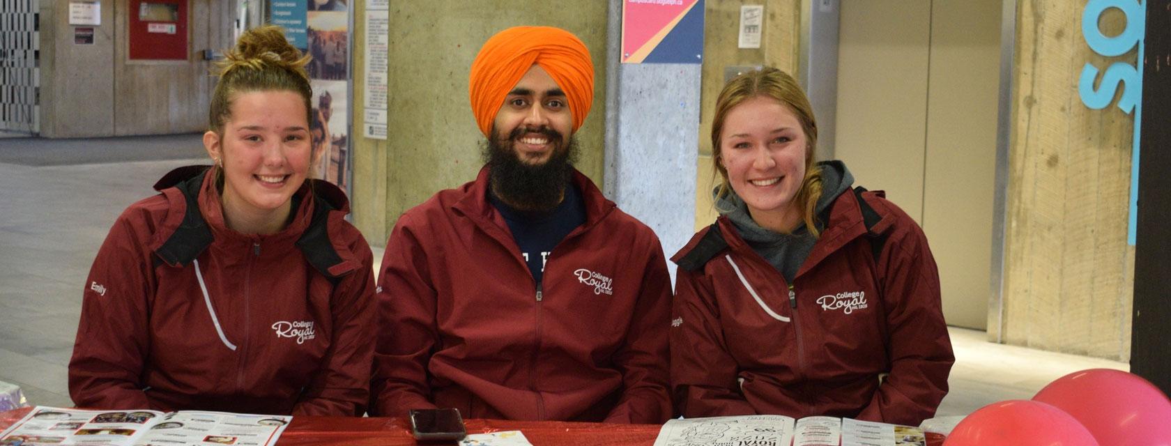 three students sitting at a registration table at the College Royal